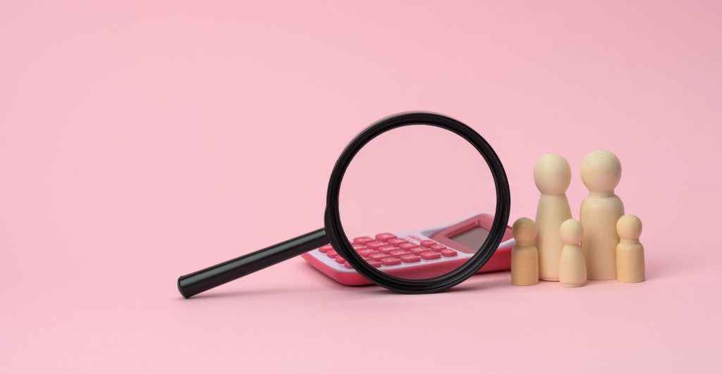 wooden figurines of little men family magnifier and calculator on a pink background